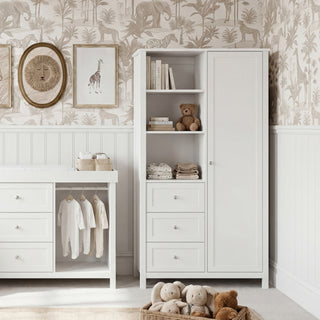 White nursery furniture with a changing table, storage cabinet, teddy bears, and animal-print wallpaper.